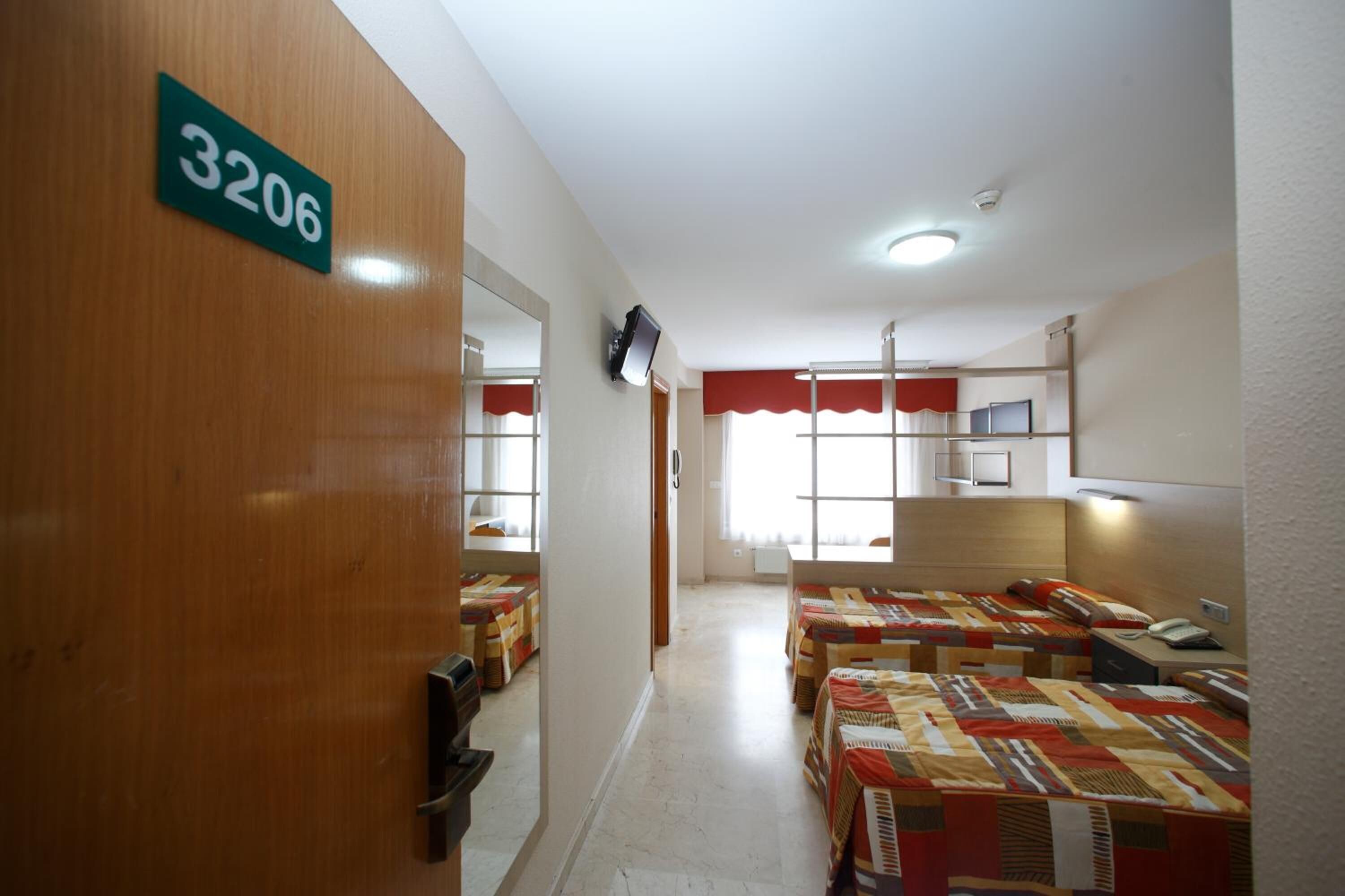 A hotel room with a number sign, a TV, and multiple beds with patterned bedding.