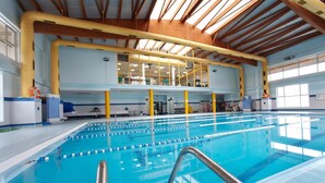 An indoor swimming pool with clear lanes, a metal handrail, and a high ceiling with wooden beams.