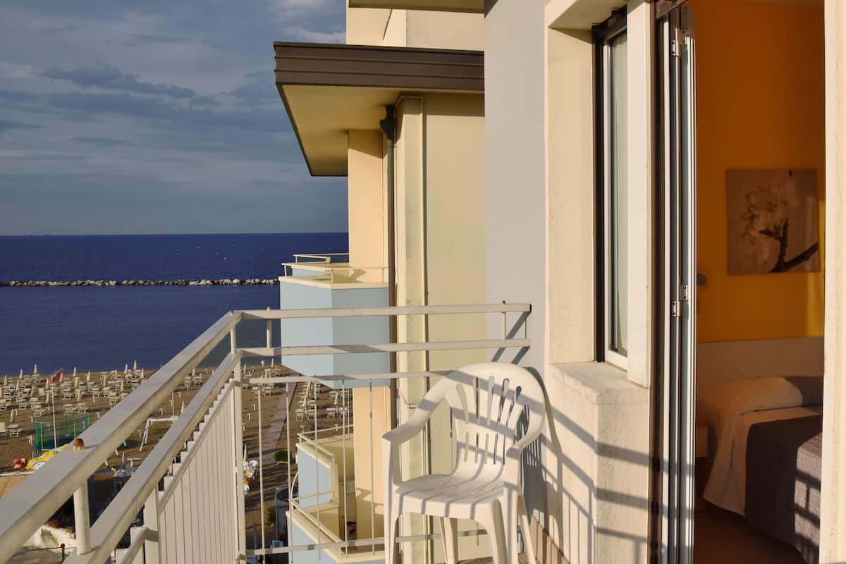 Un balcon avec vue sur la mer, une chaise en plastique blanche et un lit avec un oreiller blanc.