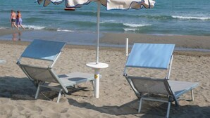 Two beach chairs and a white umbrella on a sandy beach with the ocean in the background. - Hotel Graziella (Bellaria-Igea Marina)