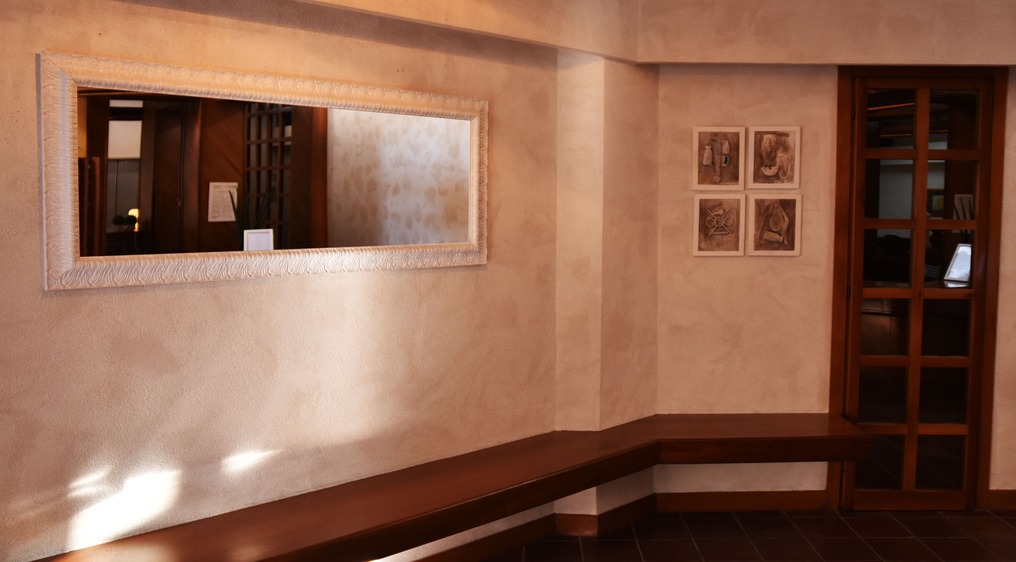 A hallway with a large mirror, a wooden bench, and a door with glass panels.