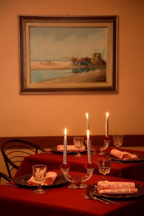 A dining table set with candles, glasses, and a painting of boats on the wall. - Hotel Graziella (Bellaria-Igea Marina)