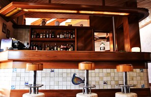 A bar area with wooden shelves stocked with bottles, a peacock tile design, and three stools with wooden tops.