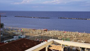 A beach with rows of sun loungers and umbrellas, a pier extending into the sea, and a building with a red roof in the foreground. - Hotel Graziella (Bellaria-Igea Marina)