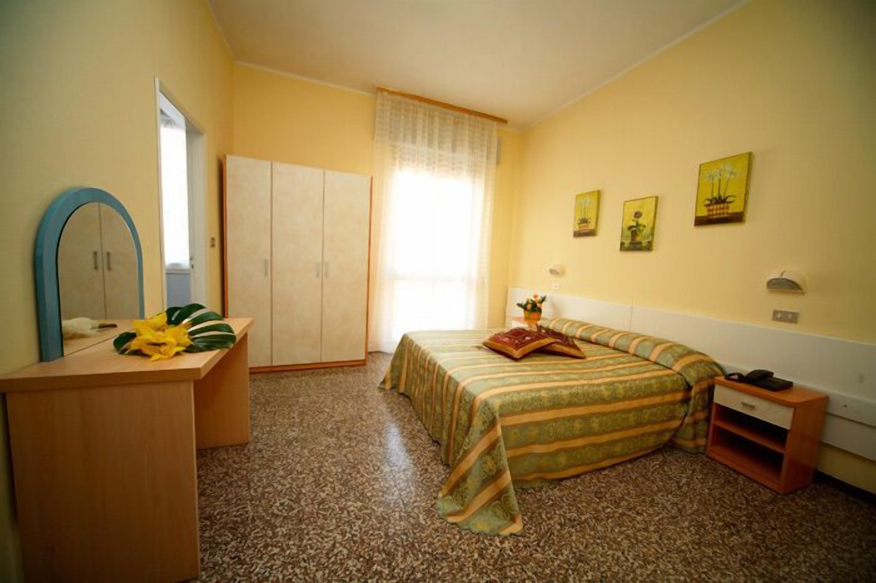Une chambre à coucher avec un lit, un bureau, une armoire et une fenêtre avec des rideaux.