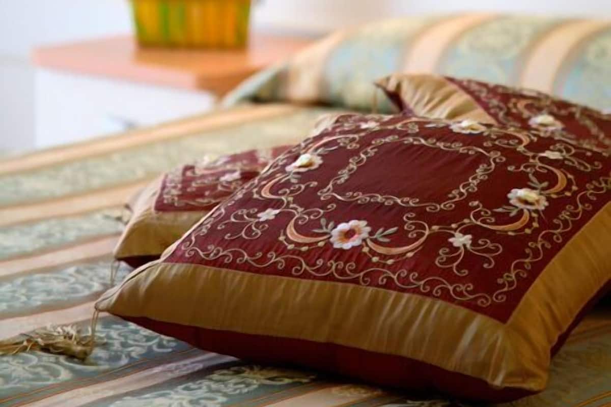 Un lit avec une literie à motifs et des coussins décoratifs, une petite table avec une plante en pot et un luminaire fixé au mur.