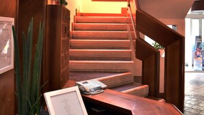 A staircase with a wooden finish, a potted plant, and a framed menu on a table. - Hotel Graziella (Bellaria-Igea Marina)