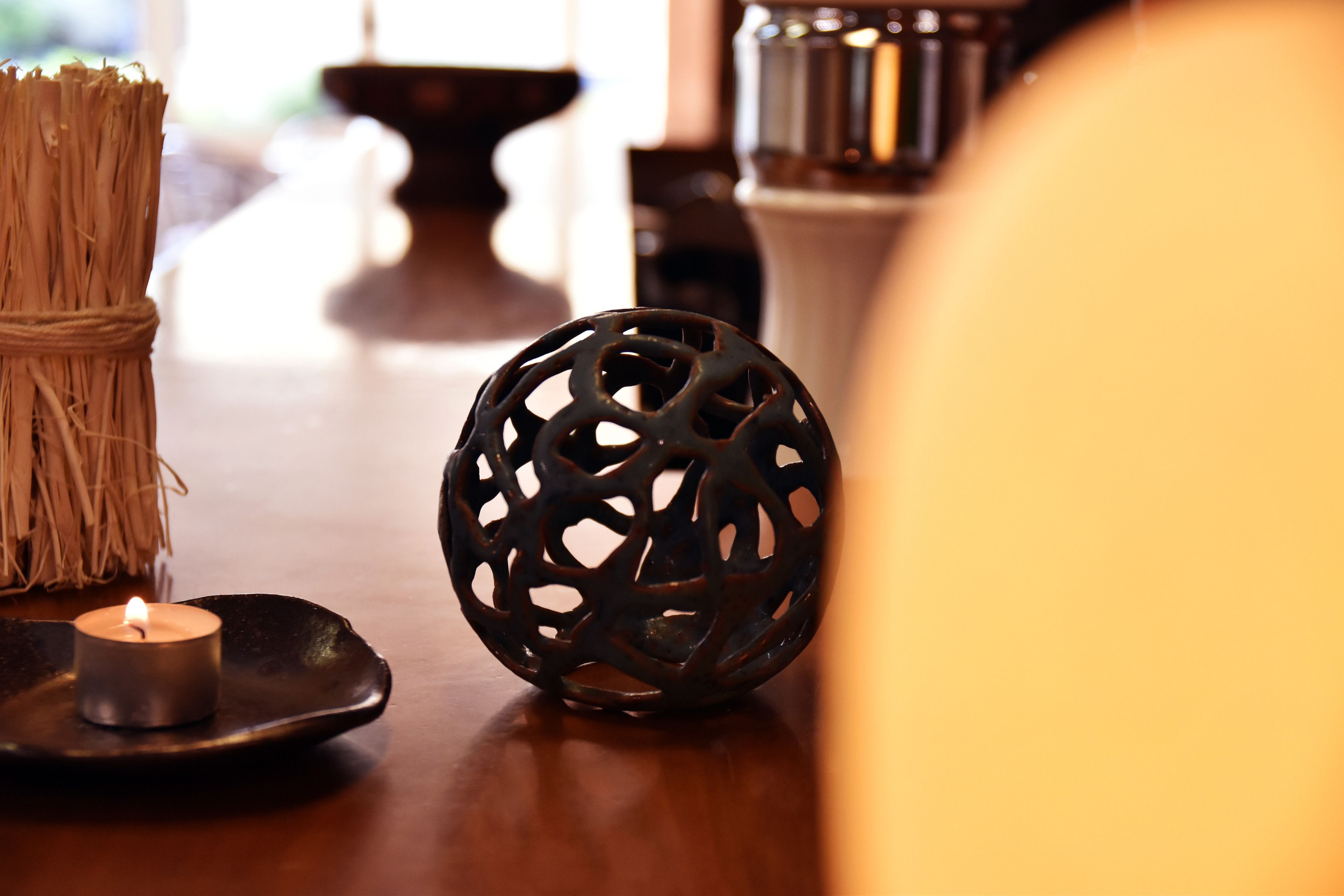 A candle on a black plate, a decorative black sphere, and a bundle of twigs on a wooden table.