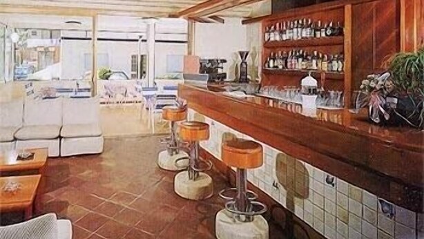 A bar area with a wooden counter, stools, and a tiled backsplash. - Hotel Graziella (Bellaria-Igea Marina)