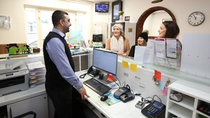 A reception desk with a computer, phone, and various papers. There is a clock on the wall and a TV screen above the desk. - Flipper Hotel Amsterdam (Amsterdam)