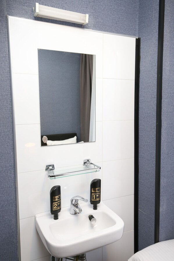 A bathroom with a white sink, two black soap dispensers, a mirror, and a towel rack. - Flipper Hotel Amsterdam (Amsterdam)
