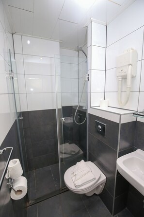 Un baño moderno con ducha envuelta en vidrio, inodoro con toalla y lavamanos.