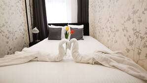 A neatly made bed with towels arranged in a heart shape, a vase with flowers, and dark curtains. - Flipper Hotel Amsterdam (Amsterdam)