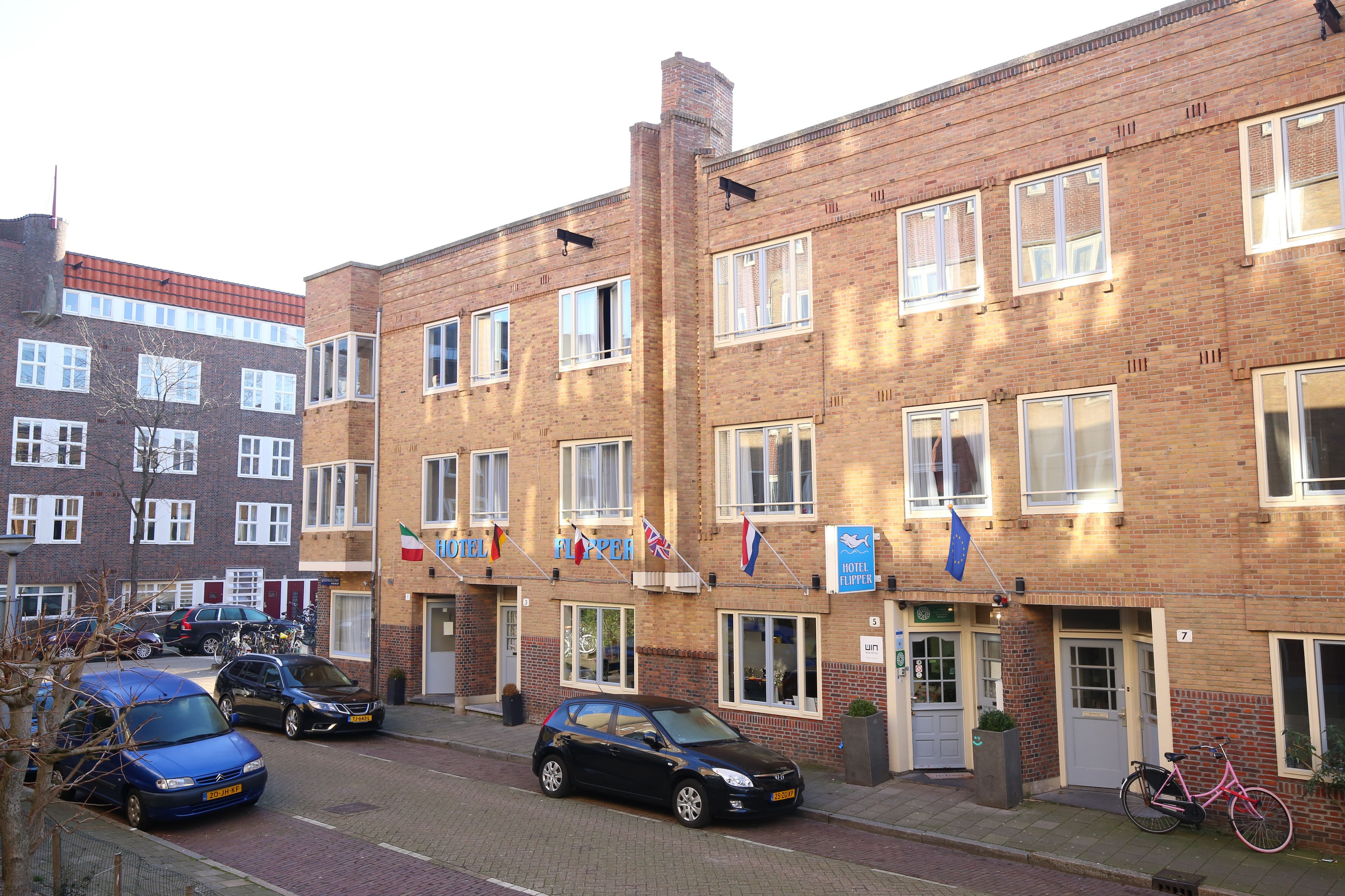 A multi-story brick building with several windows and doors, flags, and a bicycle parked outside.