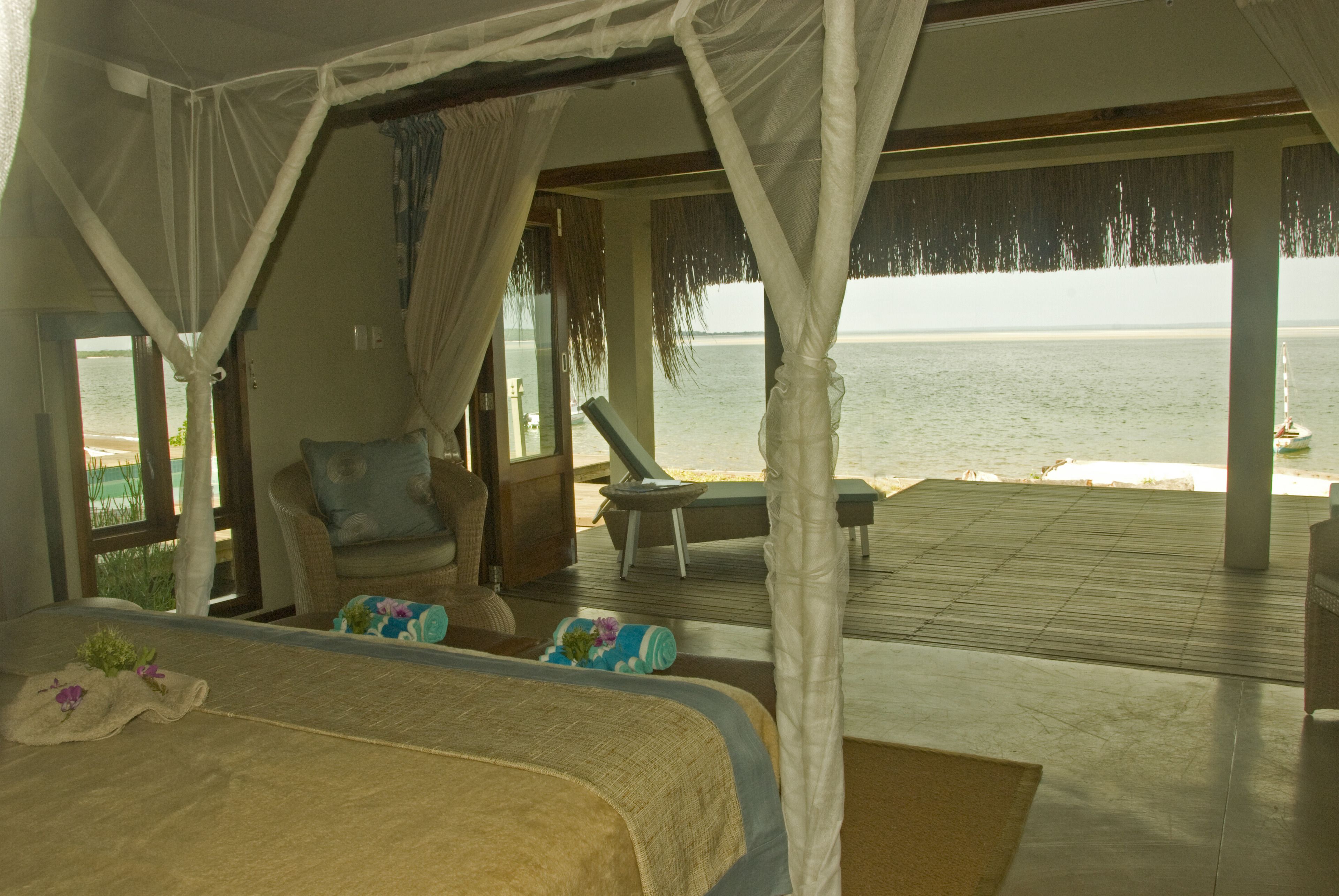 A bedroom with a bed, a chair, and a view of the sea.