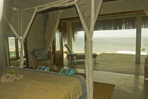 A bedroom with a bed, a chair, and a view of the sea.