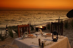 A table set for dinner on a beach with ocean views at sunset.