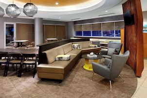 A modern lounge area with a sofa, chairs, a dining table, and a TV mounted on the wall.
