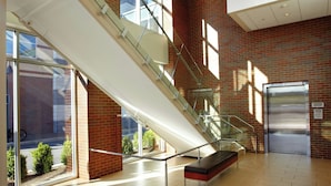A modern interior with a glass staircase, a stainless steel elevator, and a large window allowing natural light. - SpringHill Suites by Marriott Pittsburgh Bakery Square (Pittsburgh)