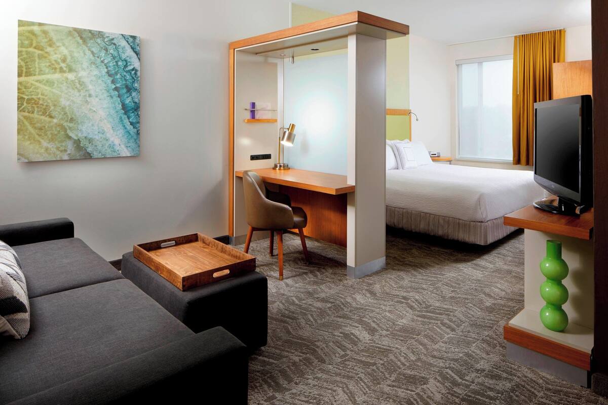A hotel room with a bed, a desk, a TV, a sofa, and a painting on the wall.