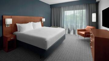 Ein Hotelzimmer mit einem großen Bett, einem Nachttisch, einem Schreibtisch, einem Sessel und einem Fernseher.