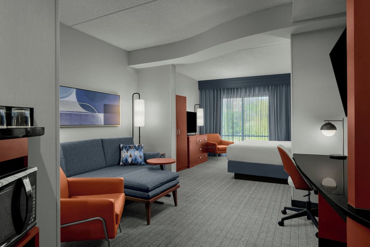 A hotel room with a sofa, a bed, a desk, a TV, and a window with curtains.