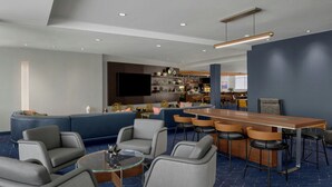 A modern hotel lobby with a blue carpet, a bar area with stools, and a seating area with sofas and chairs. - Courtyard Pittsburgh Airport Settlers Ridge (Pittsburgh)