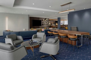 A modern hotel lobby with a blue carpet, a bar area with stools, and a seating area with sofas and chairs.