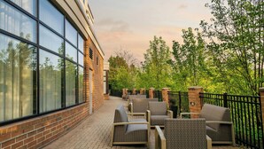 An outdoor patio with wicker furniture, a brick wall, and a glass building facade. - Courtyard Pittsburgh Airport Settlers Ridge (Pittsburgh)