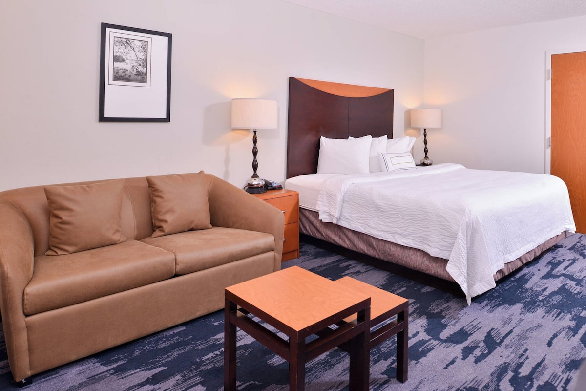 Una habitación de hotel con una cama, un sofá, una mesita y una mesita de noche con lámparas.
