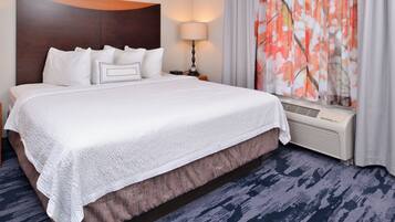 A hotel room with a large bed, a nightstand, a lamp, and a window with floral curtains.