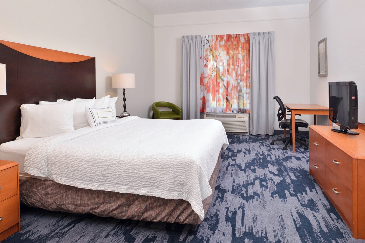 A hotel room with a large bed, a desk with a chair, a television, and a window with curtains.