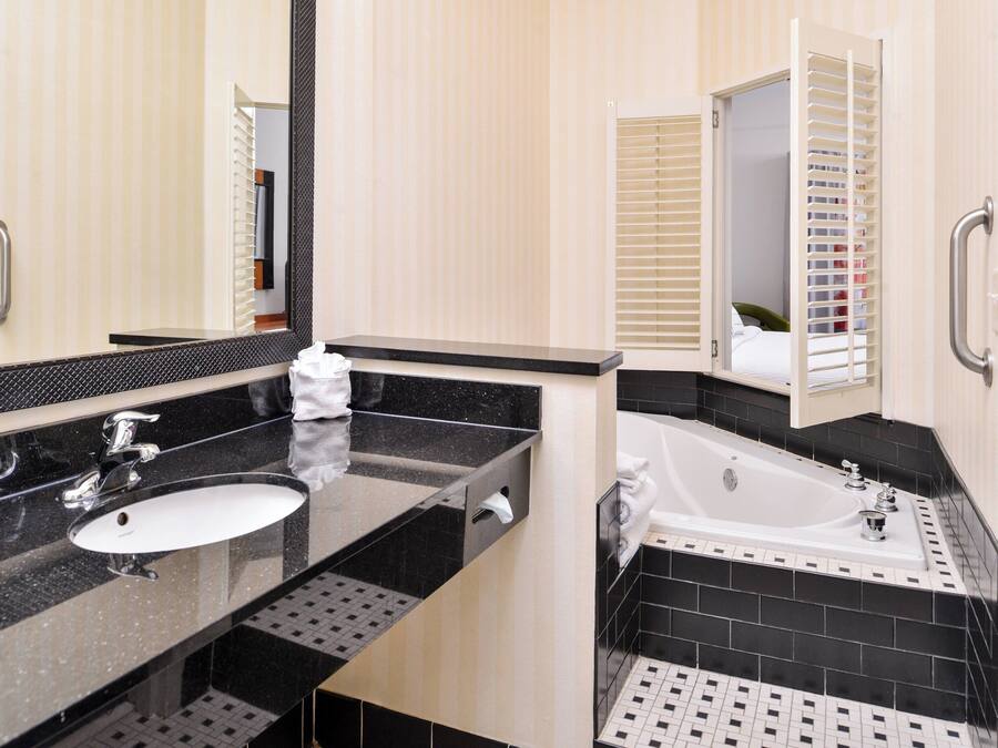 A modern bathroom with a black and white tiled floor, a sink with a mirror, and a bathtub.