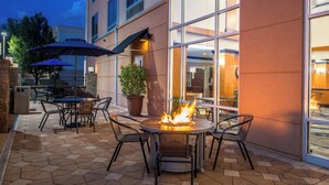 An outdoor patio with hexagonal tiles, a round table with chairs, a fire pit, and umbrellas. - Fairfield Inn & Suites by Marriott Pelham (Pelham)