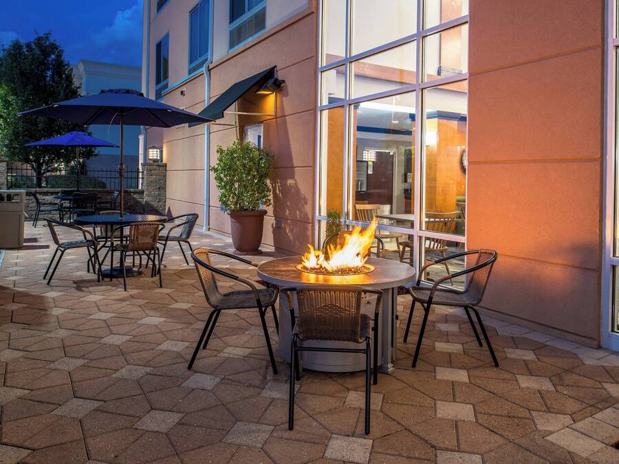 An outdoor patio with hexagonal tiles, a round table with chairs, a fire pit, and umbrellas.