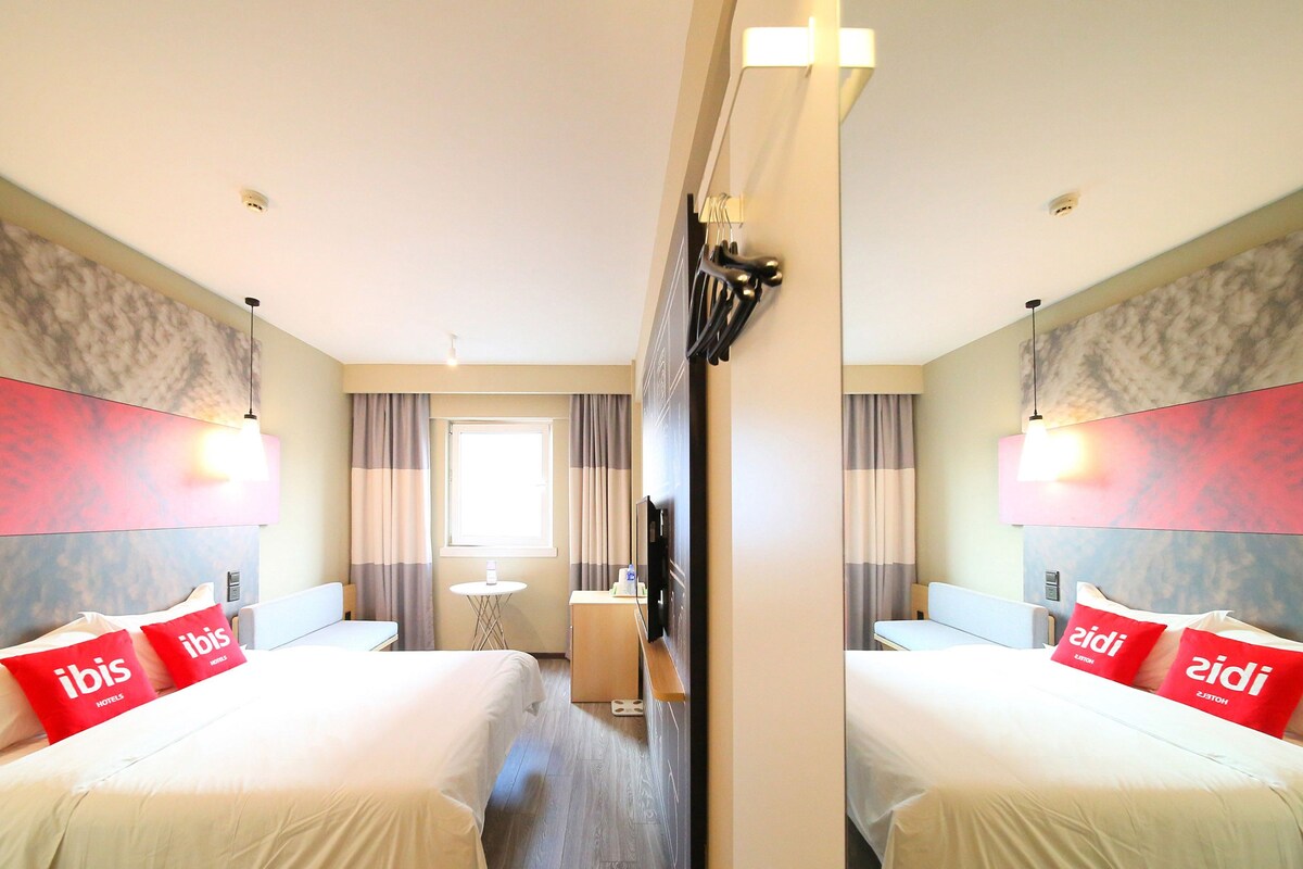 A hotel room with two beds, a small table, a TV, and a mirror.