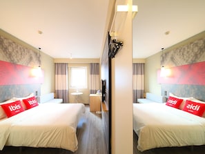 A hotel room with two beds, a small table, a TV, and a mirror.