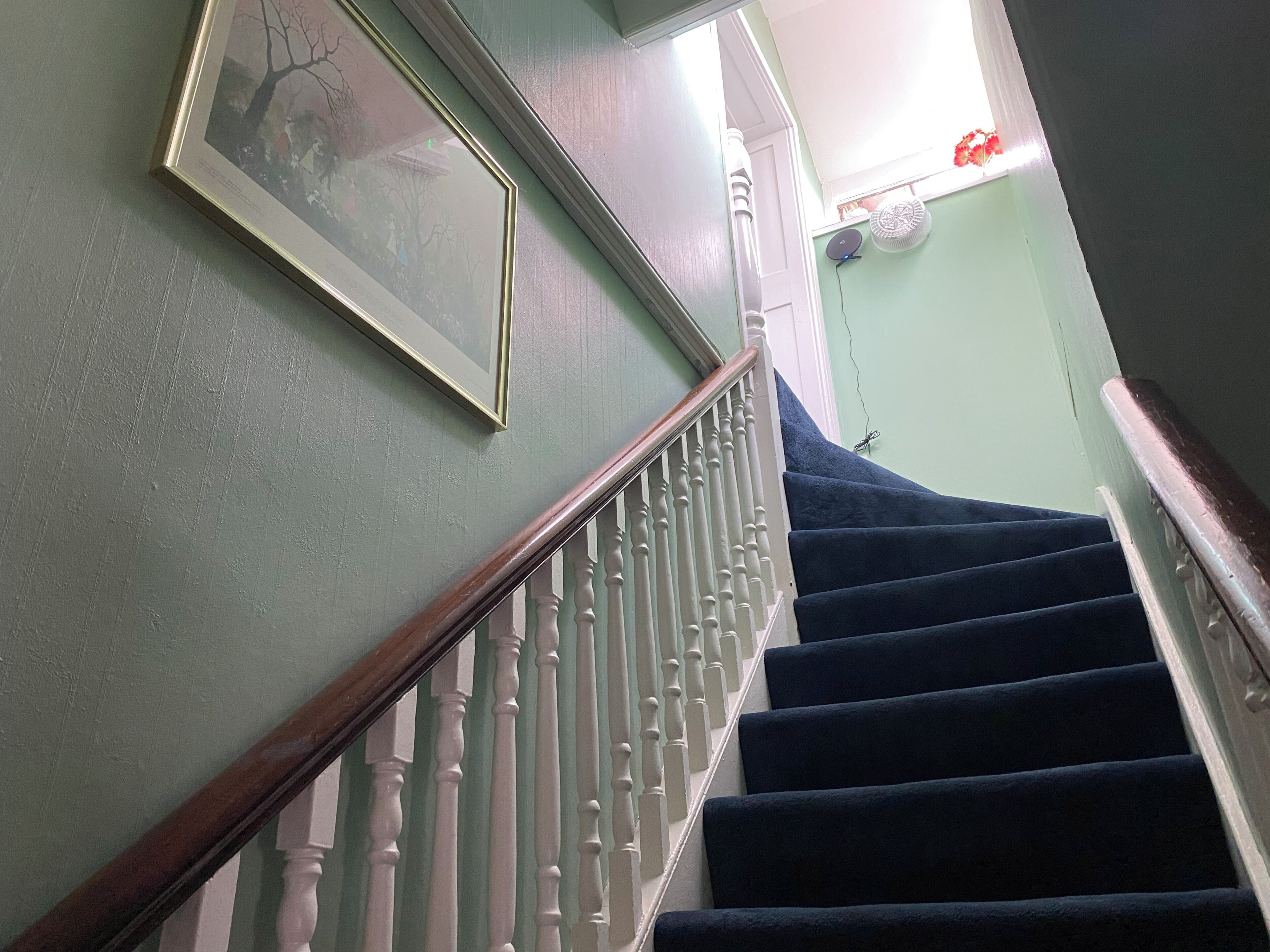 A staircase with white balusters and dark steps, a framed picture on the wall, and a fan on the wall.