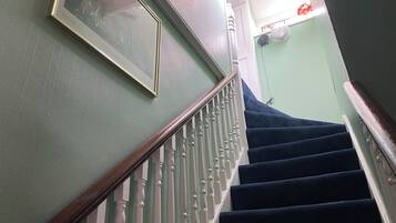 A staircase with white balusters and dark steps, a framed picture on the wall, and a fan on the wall.