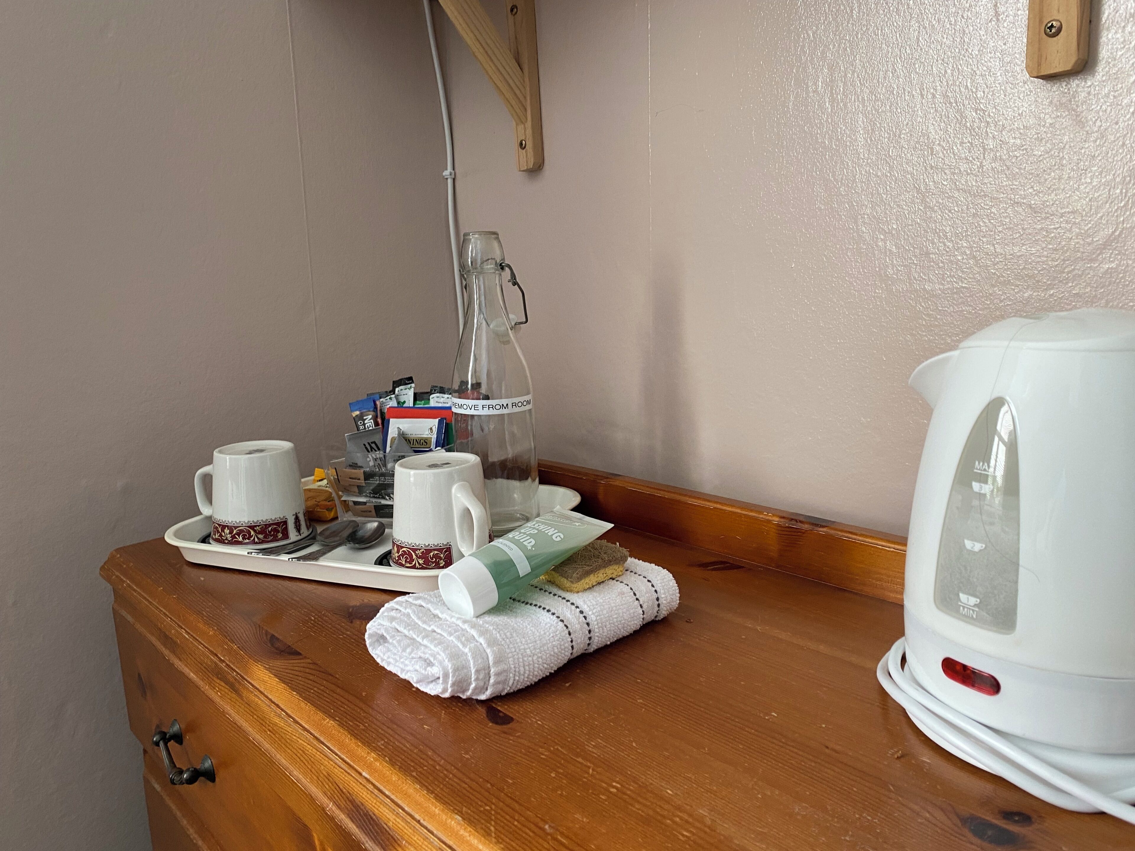 A wooden dresser with a white kettle, a glass bottle, and a tray with cups and a spoon.