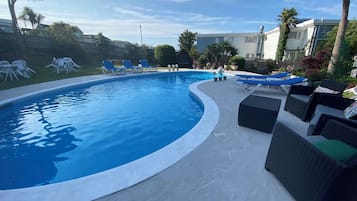 Een buitenzwembad, ligstoelen bij het zwembad