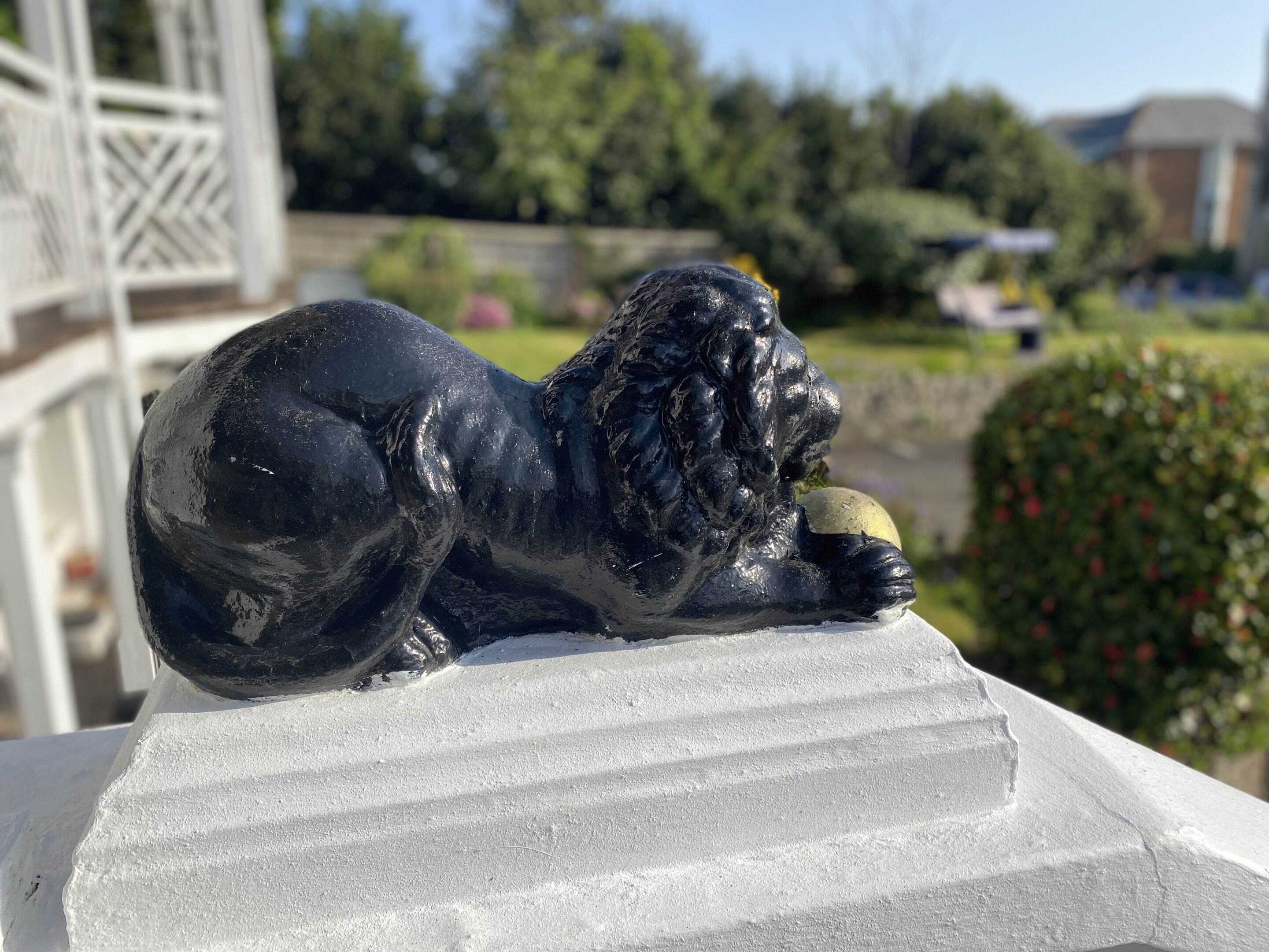 Una estatua de león negro sobre un pedestal blanco en un jardín.