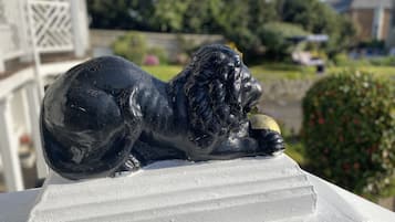 Una estatua de león negro sobre un pedestal blanco en un jardín.
