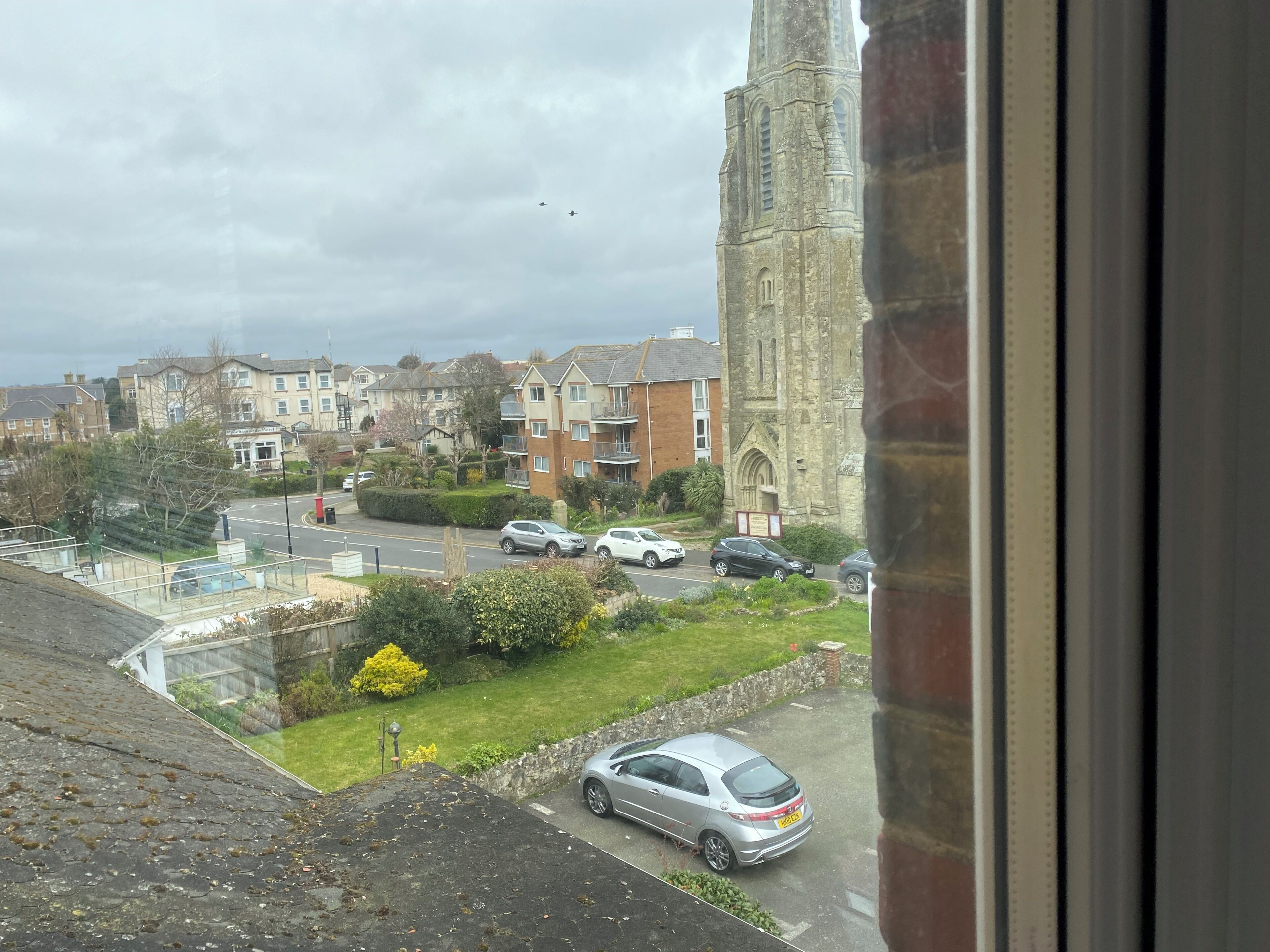A view of a residential area with a church tower, houses, and parked cars.