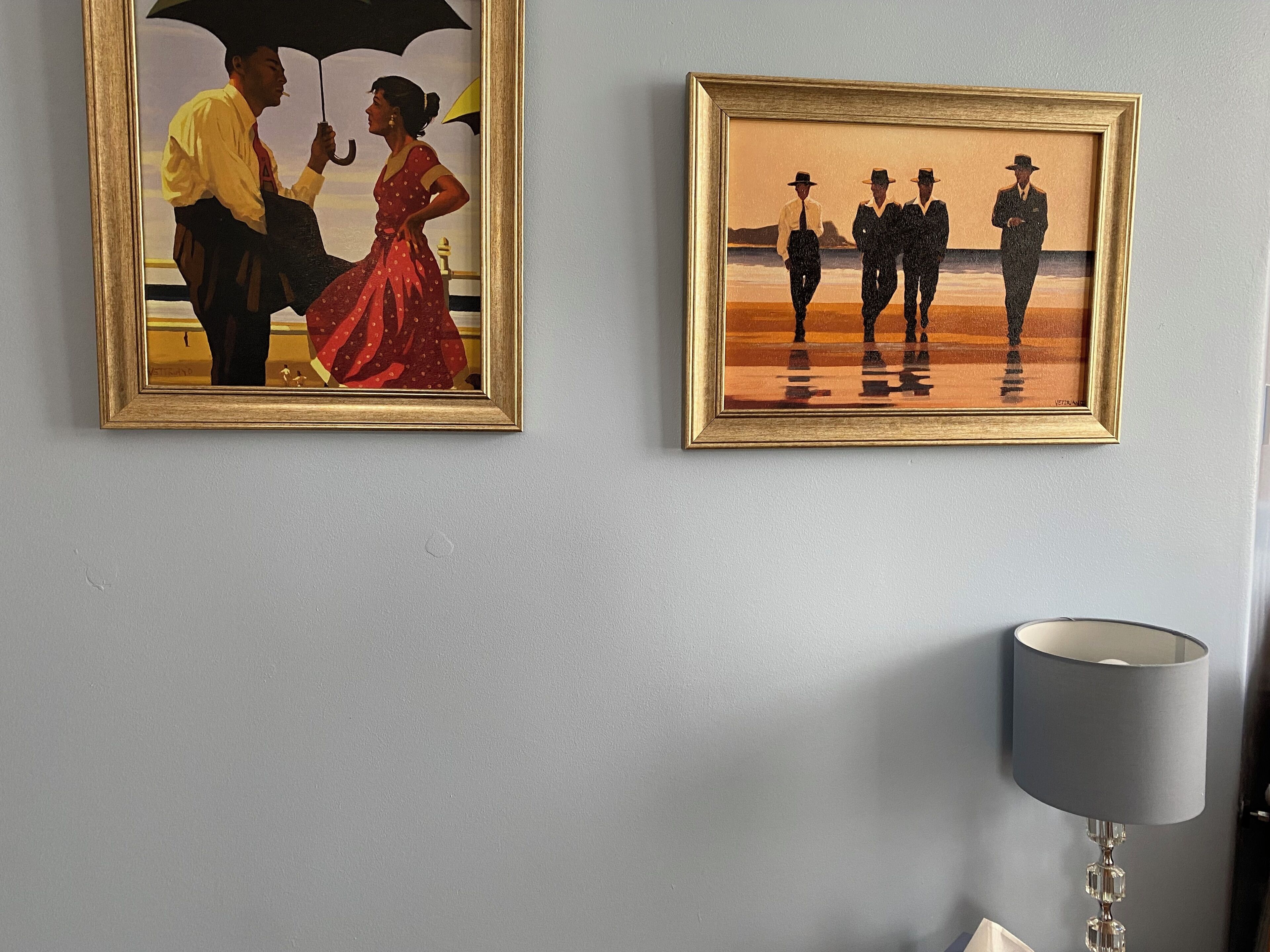 Dos cuadros enmarcados en una pared, una lámpara y una mesa.