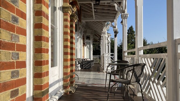 A covered outdoor area with a wooden deck, white railings, and a brick wall. - The Belmont Hotel (Shanklin)