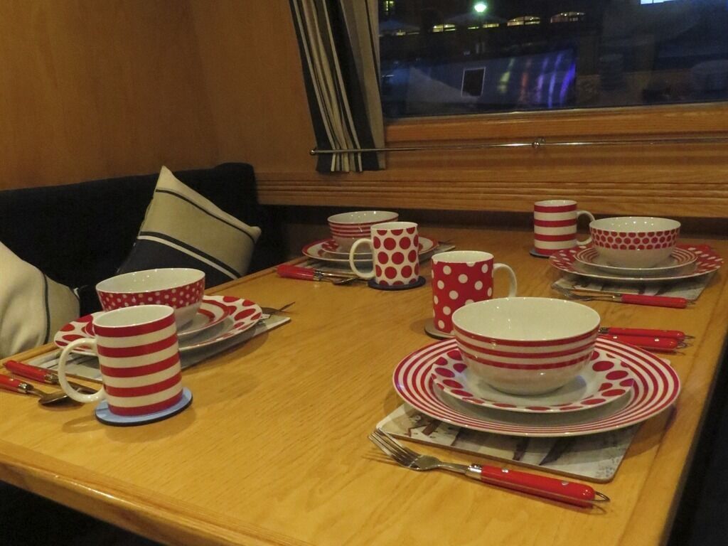 A dining table set with red and white striped tableware, including plates, bowls, and cups, with a window view in the background.