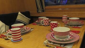 A dining table set with red and white striped tableware, including plates, bowls, and cups, with a window view in the background.