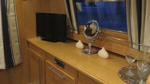 Ein kleines Zimmer mit einem Holzkästen, einem Fernseher, einem Spiegel und einem Fenster mit Vorhängen.