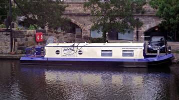 Een woonboot met een bord waarop 'Sheffield Houseboats' staat, afgemeerd bij een stenen brug.
